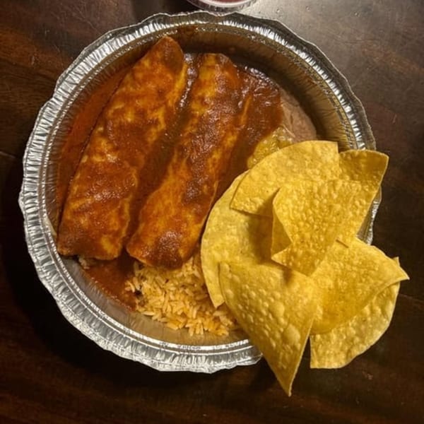 Three enchiladas covered in red sauce, rice, and tortilla chips in a foil container.