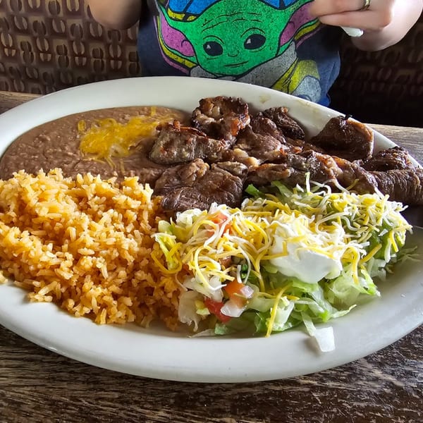 Mexican dish with steak, rice, refried beans, and a side salad with cheese and sour cream.
