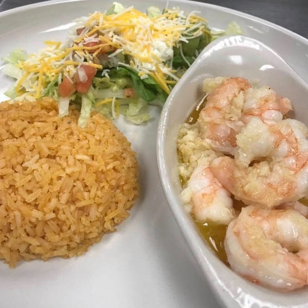Primos De Tico's Mexican dish with shrimp in sauce, rice, and a side salad with cheese.