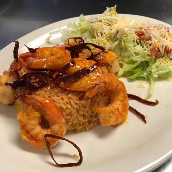 Primos De Tico's Mexican dish with shrimp, rice, and a side salad on a white plate.